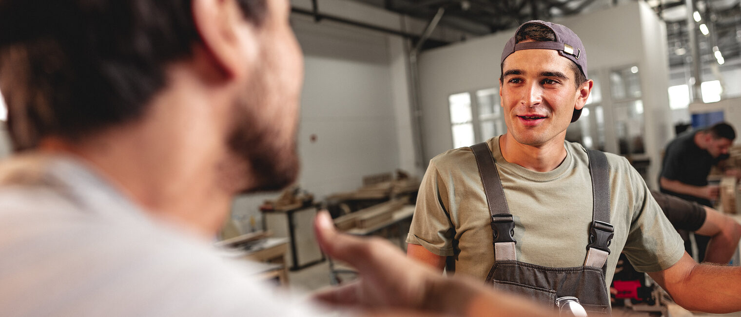 Ein Mann spricht mit einem Handwerker in einer Werkstatt.