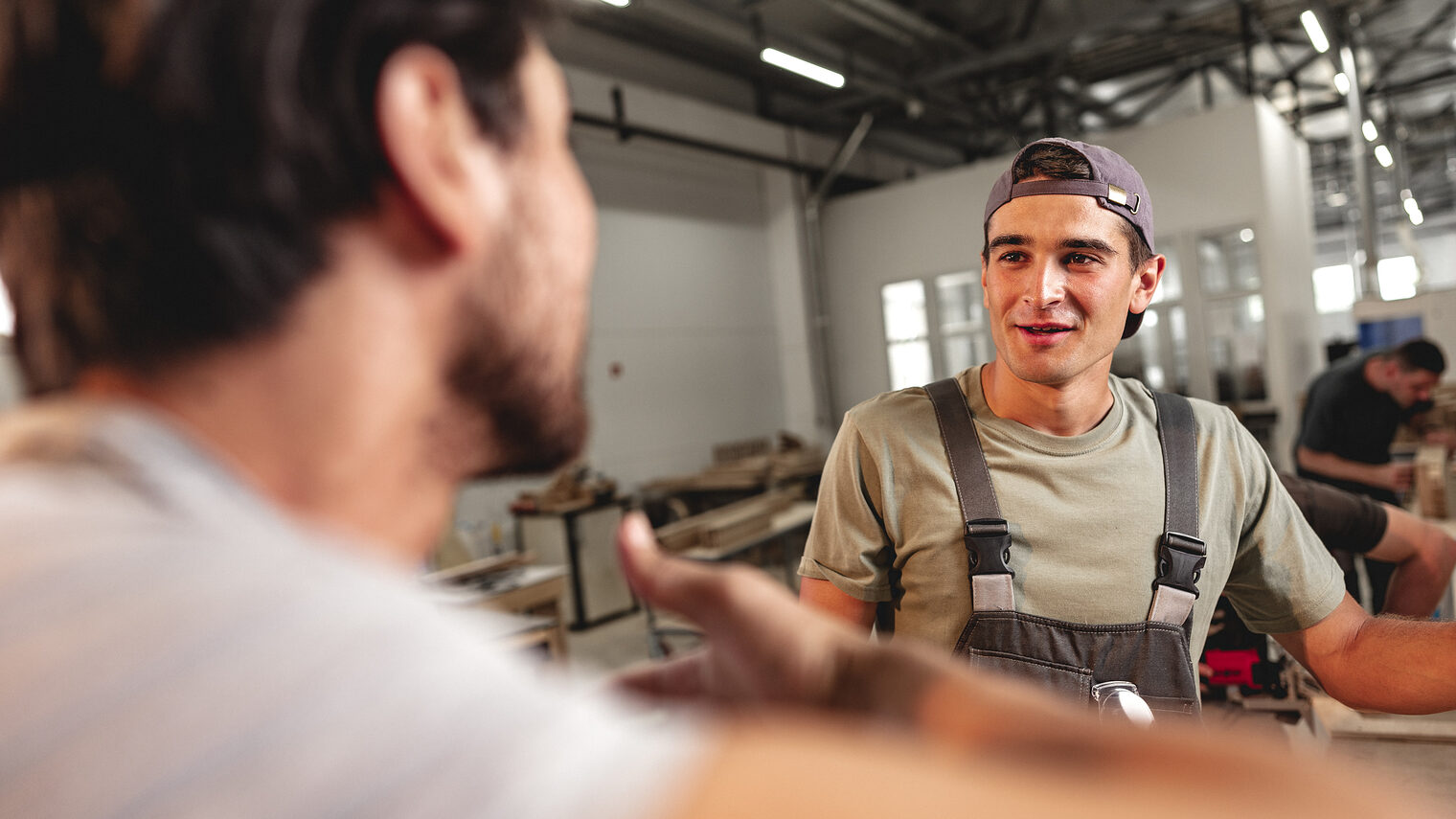 Ein Mann spricht mit einem Handwerker in einer Werkstatt.
