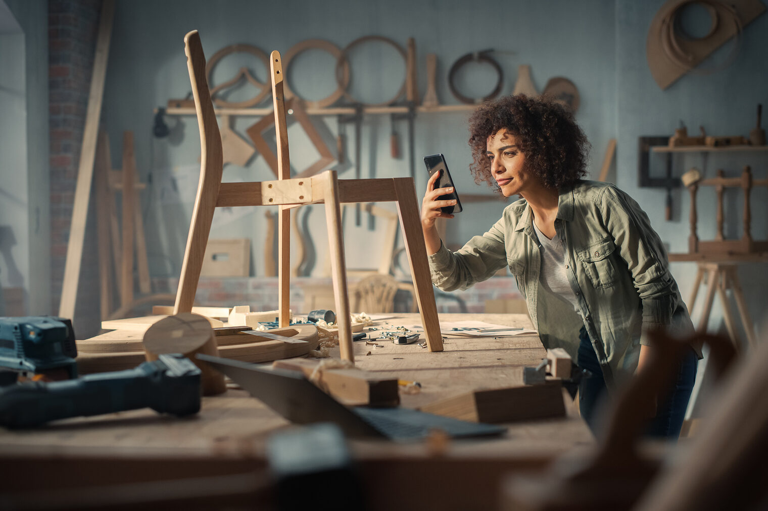 Eine Frau in einer Tischlerwerkstatt, die ein Smartphone in der Hand hält.