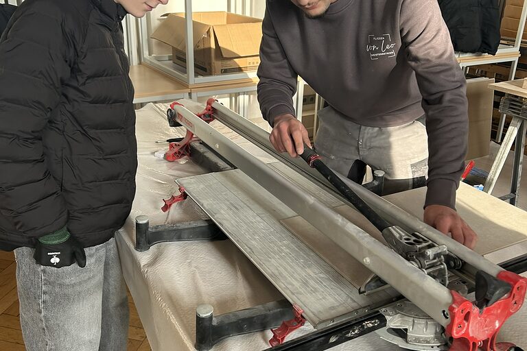Ein Schüler und ein Fliesen-, Platten- und Mosaikleger machen eine handwerkliche Übung.