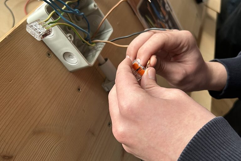 Nahaufnahme von den Händen eines Schülers, der eine elektrische Abzweigdose verdrahtet.