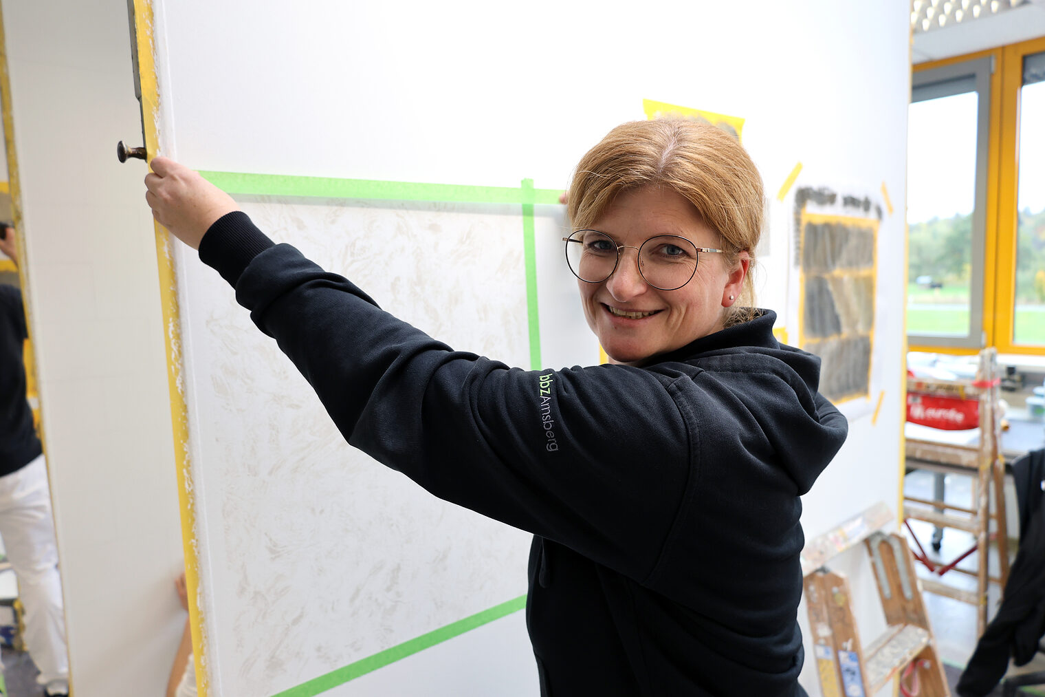 Eine Frau in einer Malerwerkstatt, die eine Fläche abklebt.