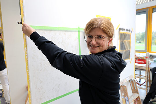 Eine Frau in einer Malerwerkstatt, die eine Fläche abklebt.