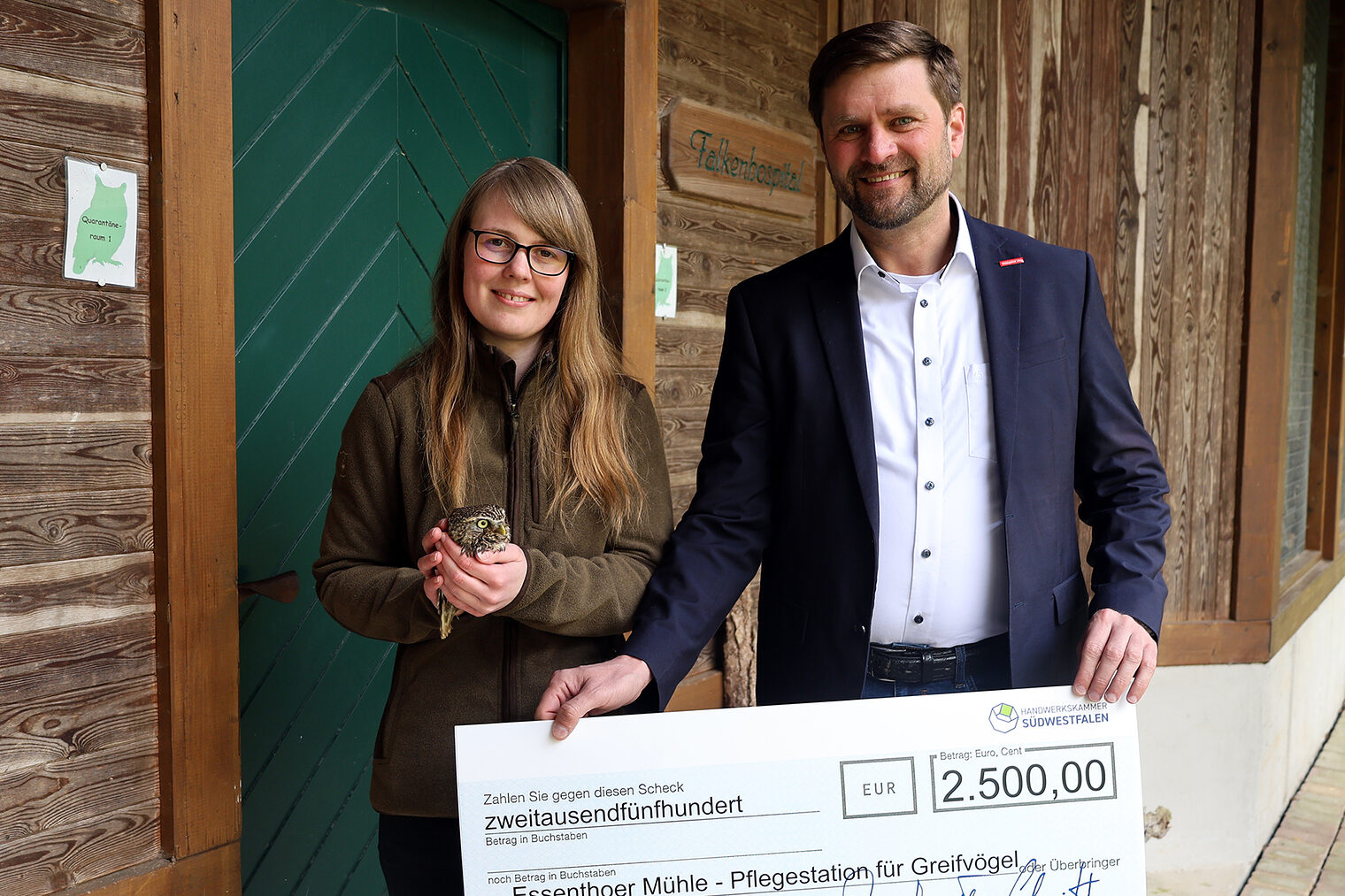 Hendrik Schmitt (HwK Südwestfalen) überreicht einen Scheck an Anna Reichel (Vogelpflegestation). Reichel hält einen Waldkauz.