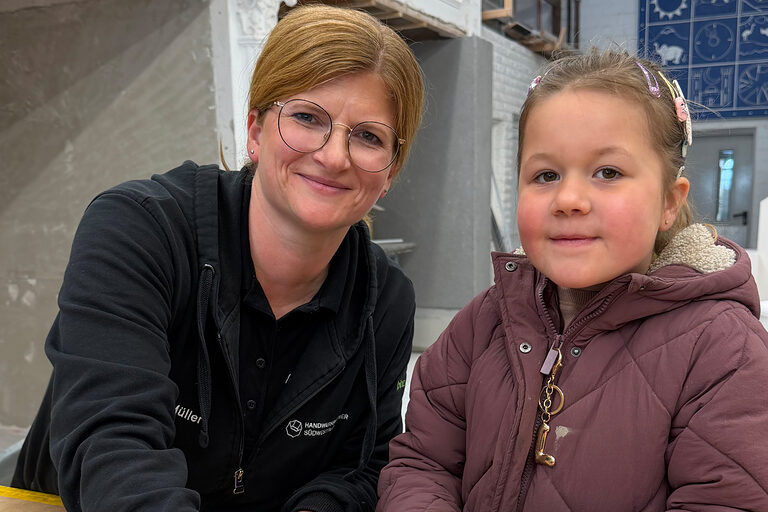 Eine Frau und ein Mädchen im Kindergartenalter in einer Fliesenlegerwerkstatt.
