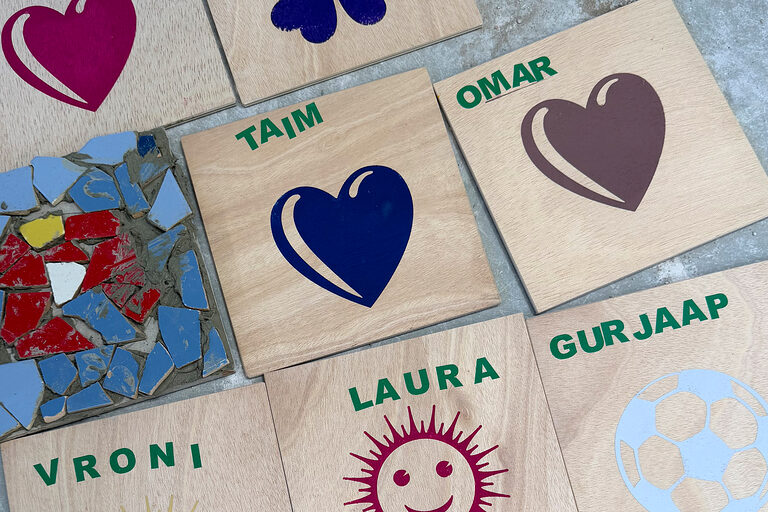 Verschiedene Bilder auf Holzplatten sowie ein Mosaikbild liegen auf einem Tisch.