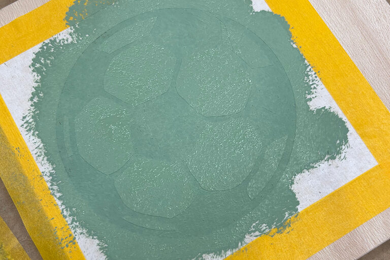 Nahaufnahme eines Bildes. Ein grün eingefärbter Fußball in einem gelben Rahmen.