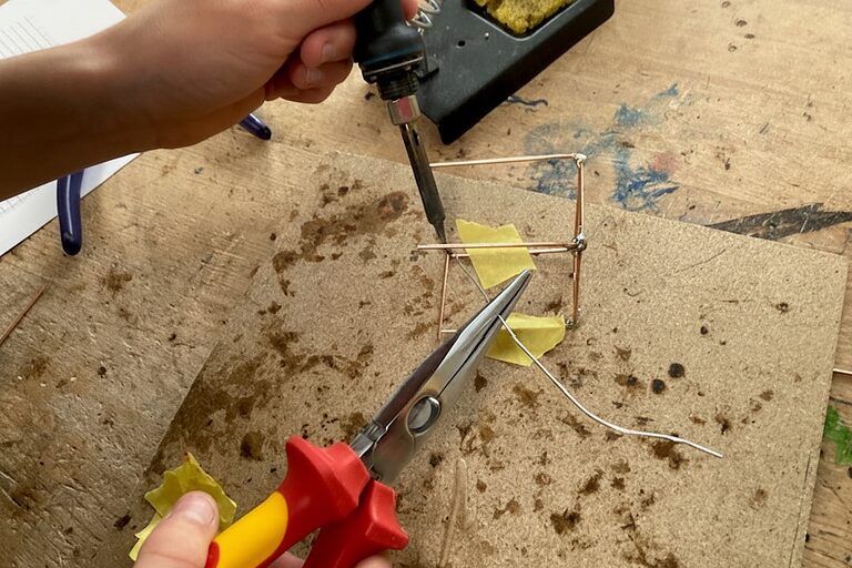 Ein Schüler lötet kleine Metalldrähte zusammen.