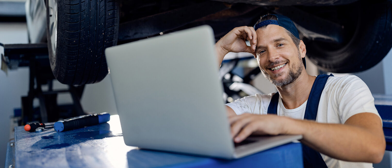 Ein Automechaniker steht vor einem Laptop in seiner Werkstatt.