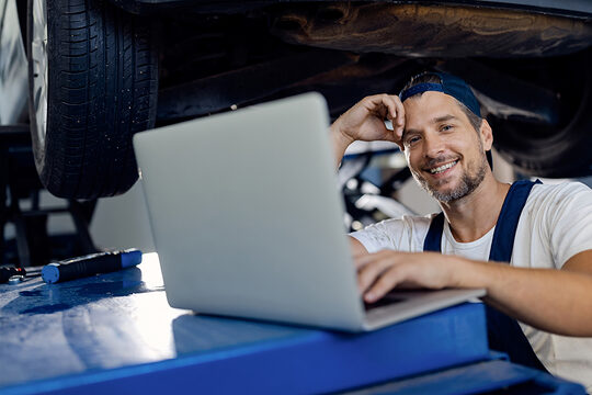 Ein Automechaniker steht vor einem Laptop in seiner Werkstatt.