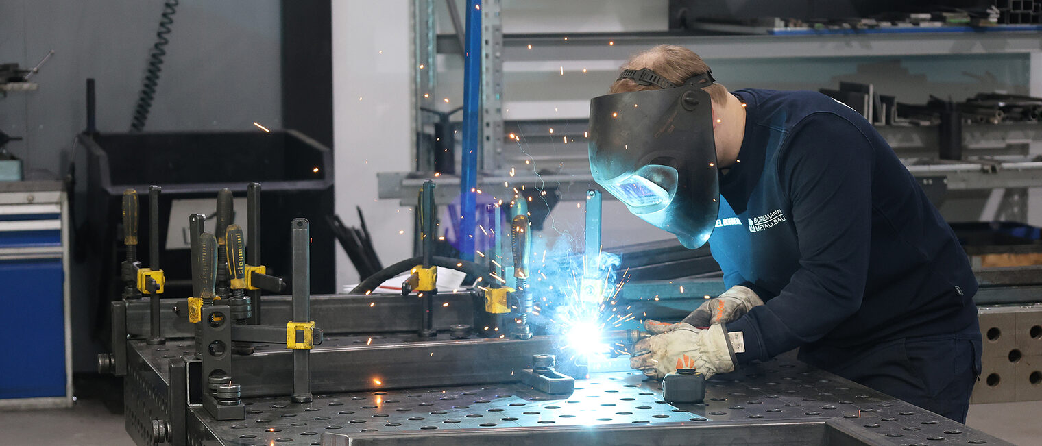 Ein Metallbauer beim Schweißen von Metallteilen in einer Werkstatt.