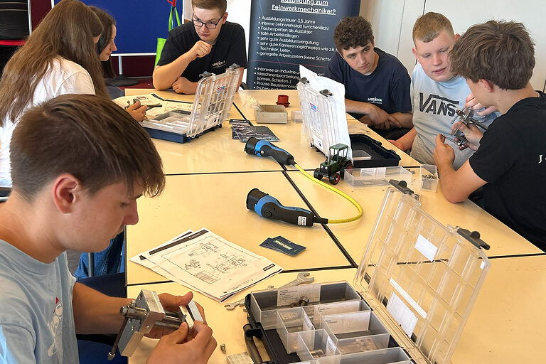 Schülerinnen und Schüler sitzen an einem Tisch und bauen Schraubstöcke zusammen.