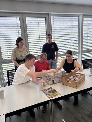Mehrere Teilnehmerinnen und Teilnehmer eines Workshops bauen ein Modell eines Hauses.