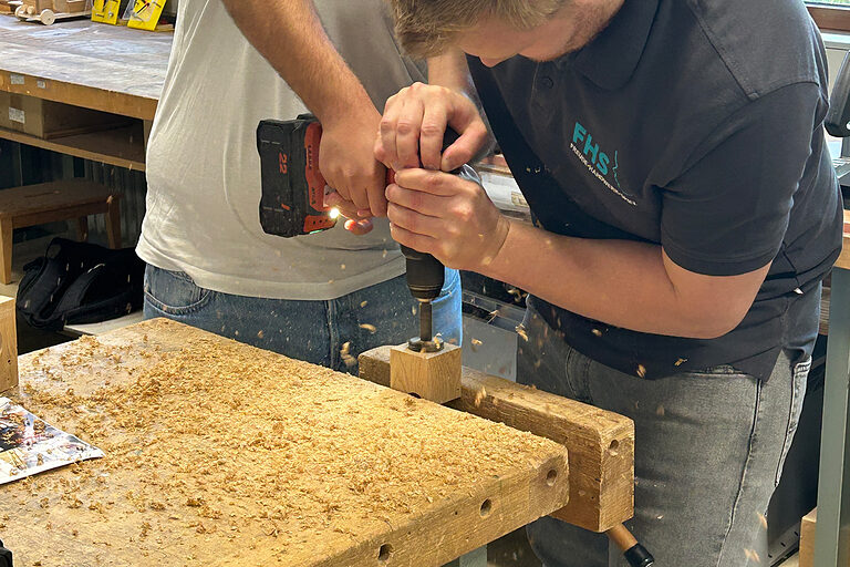 Ein Schüler und ein Vertreter eines Handwerksbetriebs boren ein Stück Holz an.