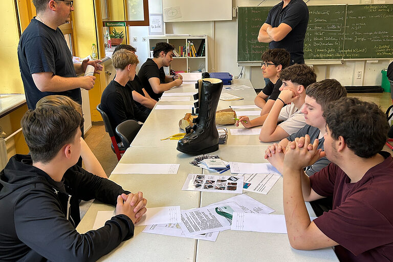 Schüler sitzen an einem langen Tisch und betrachten einen orthopädischen Schuh.