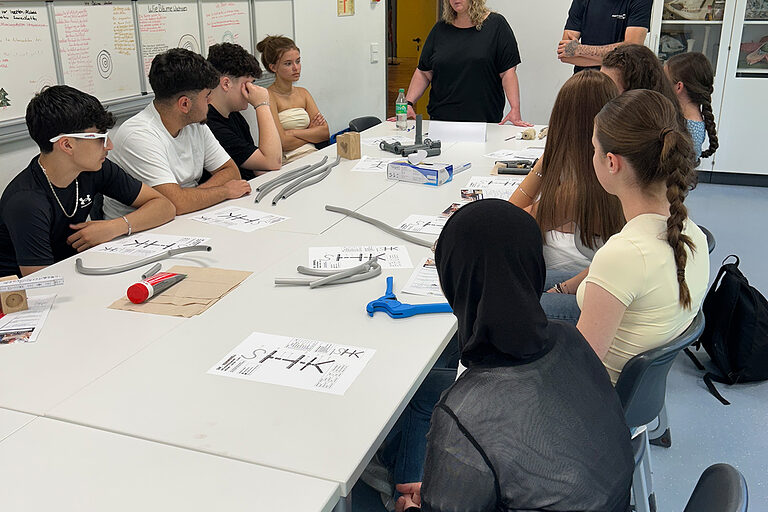 Zwei Betriebsverteter halten einen Vortrag vor Schülern in einem Klassenraum.