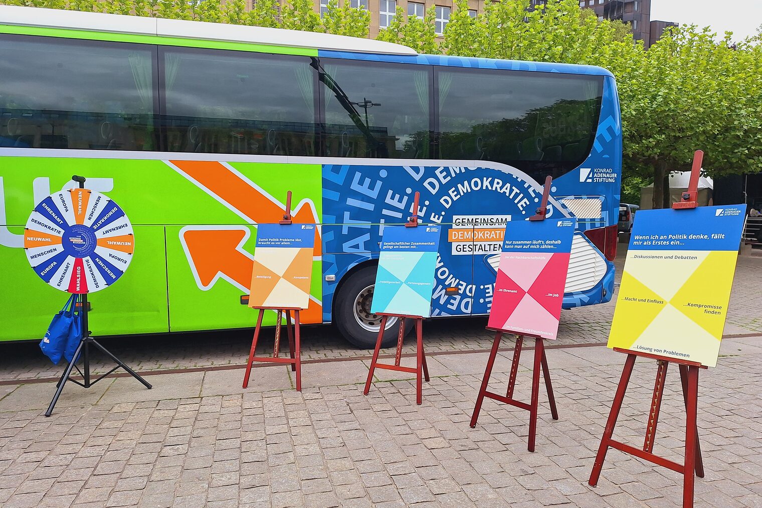 Ein Bus auf einem Parkplatz. Der Bus ist mit "Gemeinsam Demokratie gestalten" beschriftet. Vor dem Bus stehen Schaubilder.