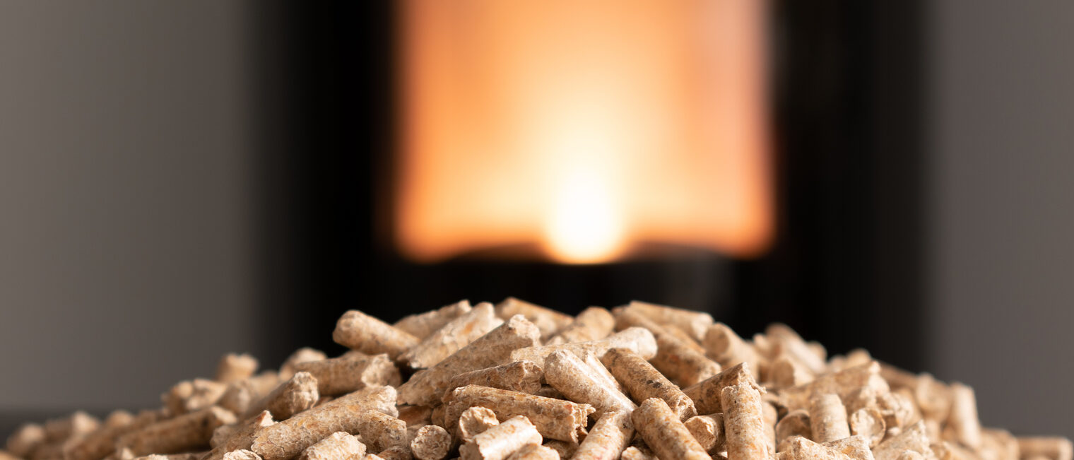 Ein Haufen Holzpellets, im Hintergrund ein Ofen.