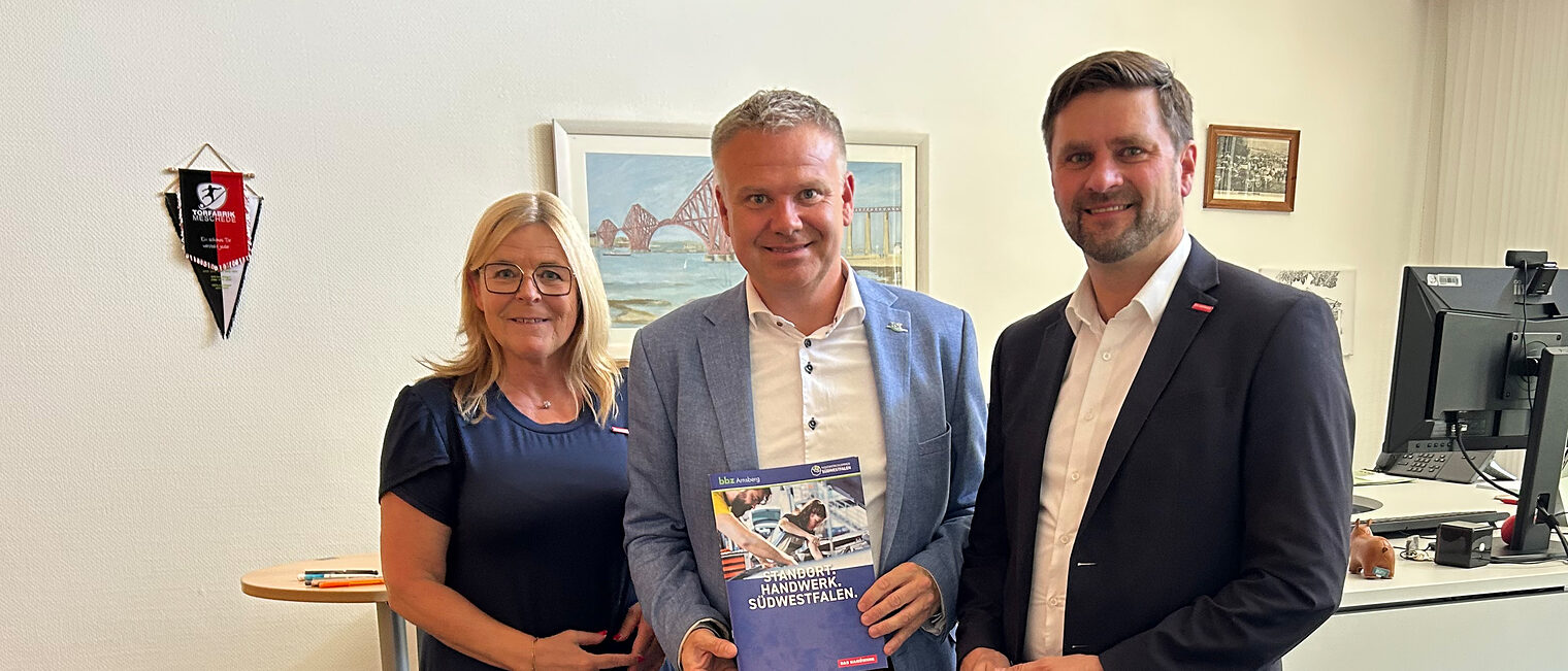 Gruppenbild mit Uta Neumeister, Thomas Grosche und Hendrik Schmitt. Grosche, in der Mitte stehend, hält eine Broschüre.