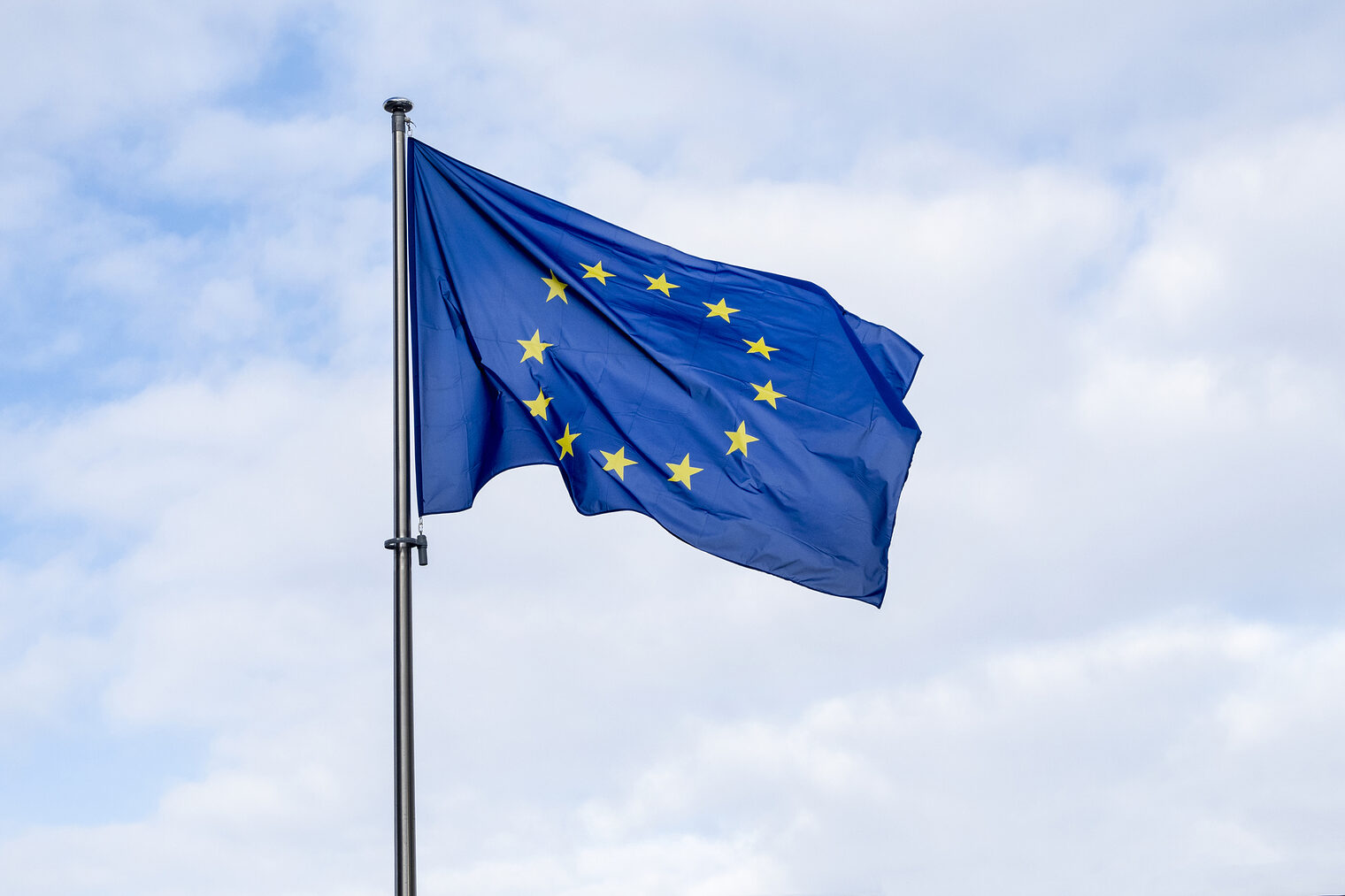 Aufnahme einer EU-Flagge vor einem teilweise bewölktem Himmel.
