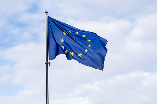 Aufnahme einer EU-Flagge vor einem teilweise bewölktem Himmel.