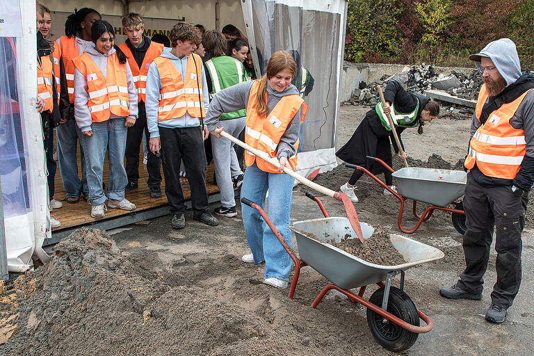 Eine Schülerin schaufelt Sand in eine Schubkarre bei der Heckmann Bau Handwerkschallenge