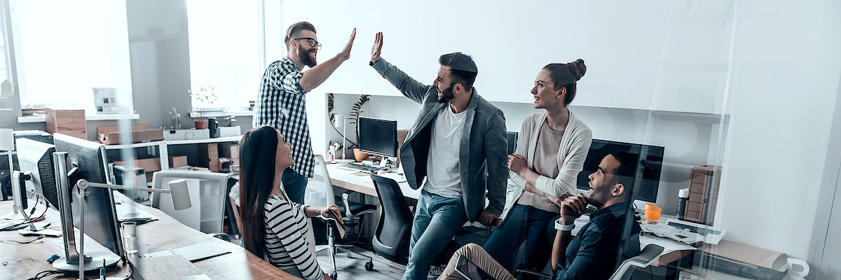 Two cheerful young business people giving high-five while their colleagues looking at them and smiling Schlagwort(e): Men, Women, People, Corporate Business, Modern, Success, Expertise, High-Five, Celebration, Group Of People, Office, Business, Creative Occupation, Multi-Ethnic Group, New Business, Solution, Working, Meeting, Brainstorming, Design Studio, Business Finance And Industry, Cooperation, Technology, Professional Occupation, Togetherness, Unity, Discussion, Smart Casual, Business Casual, Teamwork, Team, Ideas, Planning, Strategy, Coworker, Standing, Sitting, Leaning, Indoors, Talking, Smiling, Happiness, Gesturing, Beard, Transparent, Glass-Material