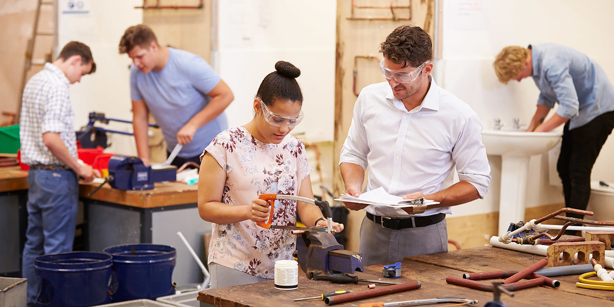 Teacher Helping College Students Studying Plumbing Wearing Protective Goggles Schlagwort(e): 16-17 Years, 18-19 Years, 30s, African Descent, African Ethnicity, Assistance, Caucasian, Cheerful, Classroom, Craft, Education, Female, Four People, Horizontal, Instructor, Learning, Little Boys, Male, Men, Occupation, People, Pipe, Plumber, Protective Eyewear, Saw, Sawing, Skill, Smiling, Student, Studying, Support, Teacher, Teenage Girls, Teenager, Togetherness, Trainee, Training, University, Water Pipe, Work Tool, Working, Workshop