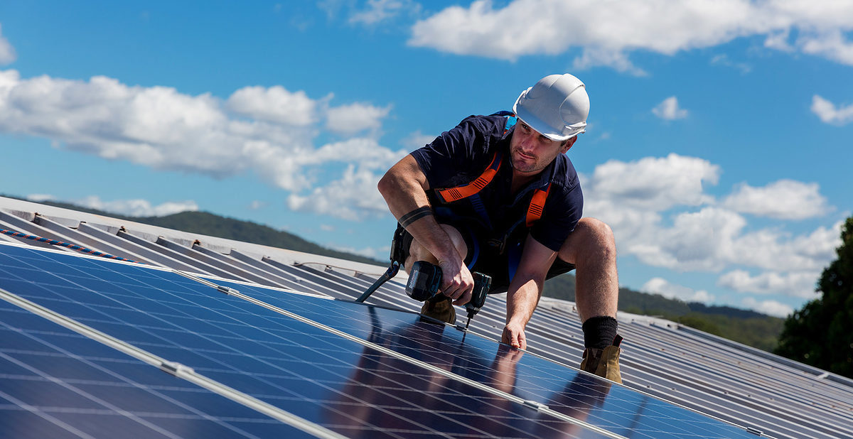 Solar panel installer with drill installing solar panels on roof on a sunny day Schlagwort(e): installer, renewable