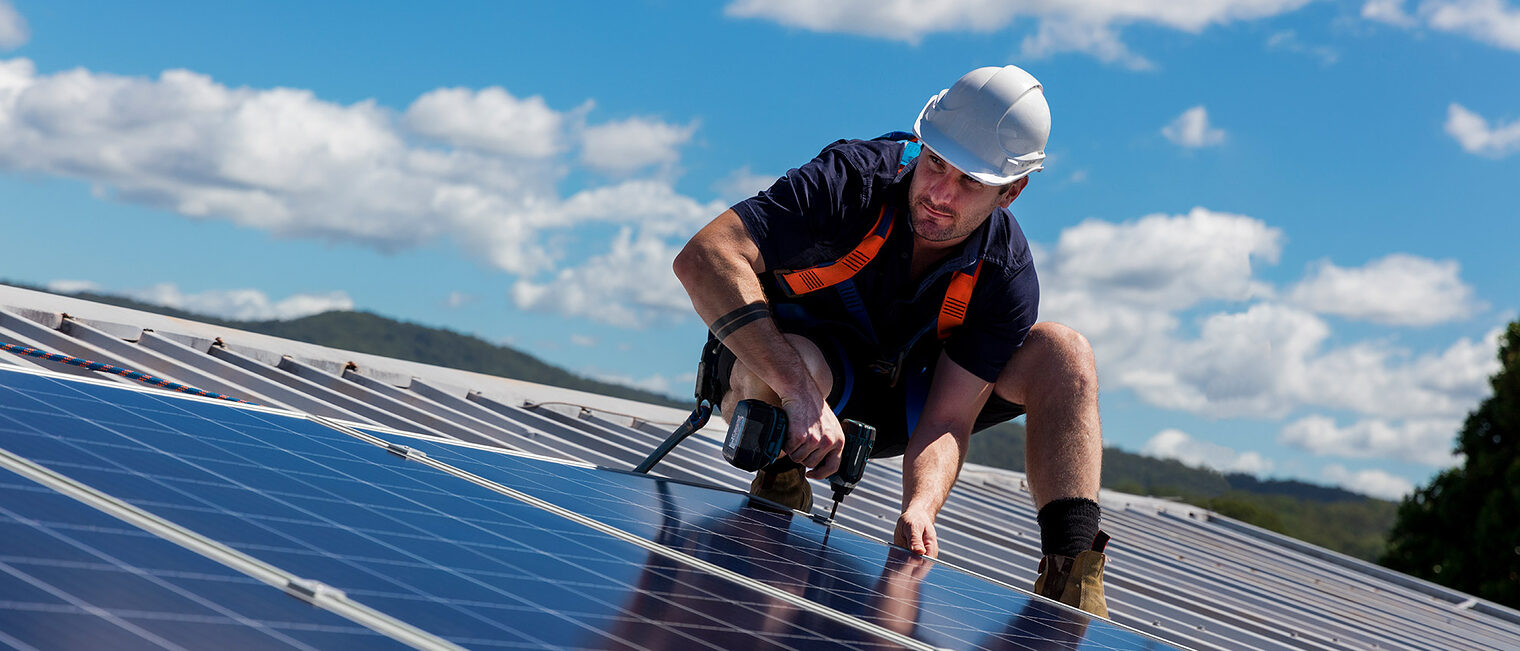Solar panel installer with drill installing solar panels on roof on a sunny day Schlagwort(e): installer, renewable